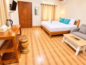 A hotel room with a wooden bed, a sofa, a wooden table, and a small wooden stool.