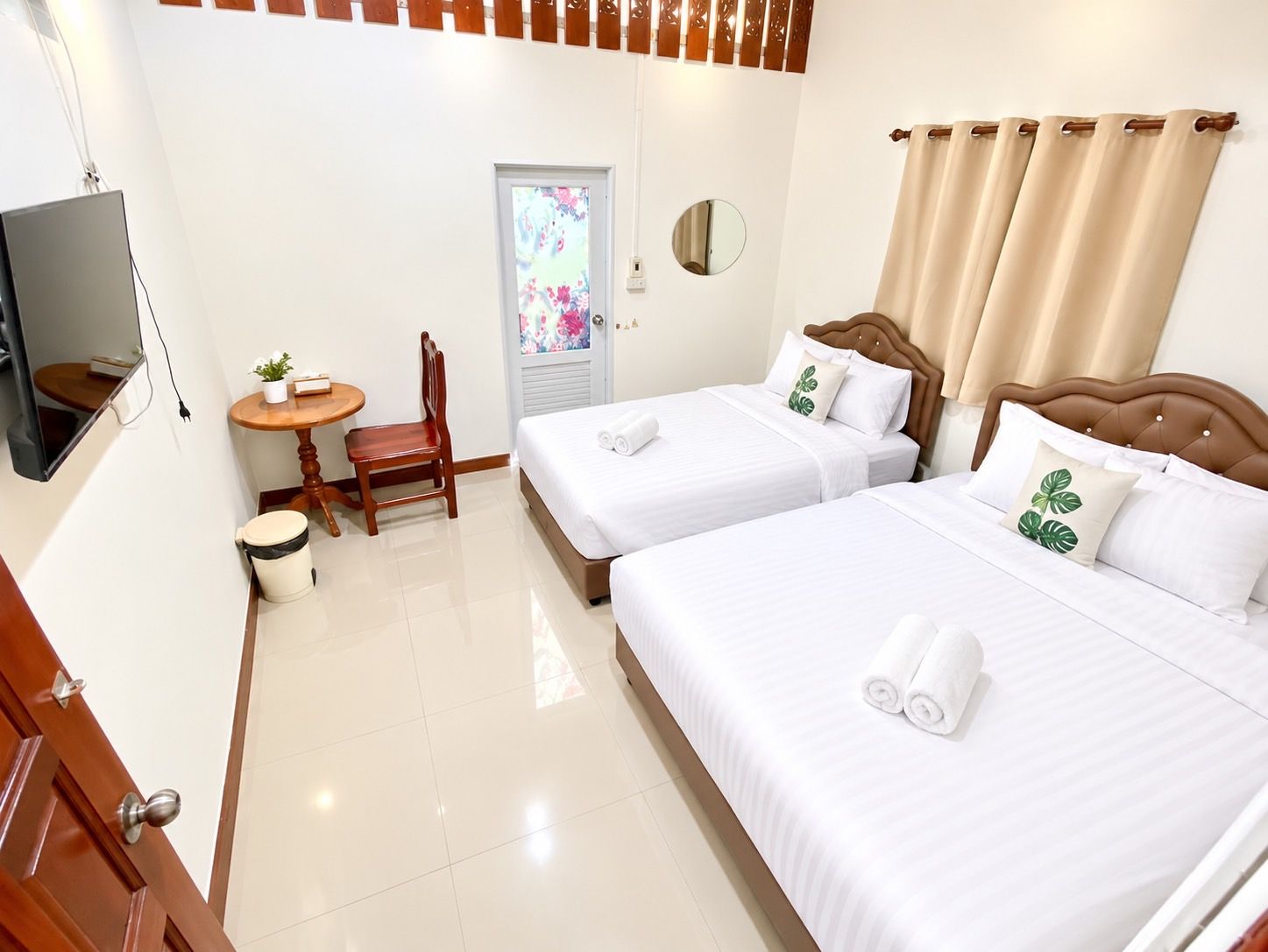 A hotel room with two beds, a small table with a chair, a television, and a door with a frosted glass window.
