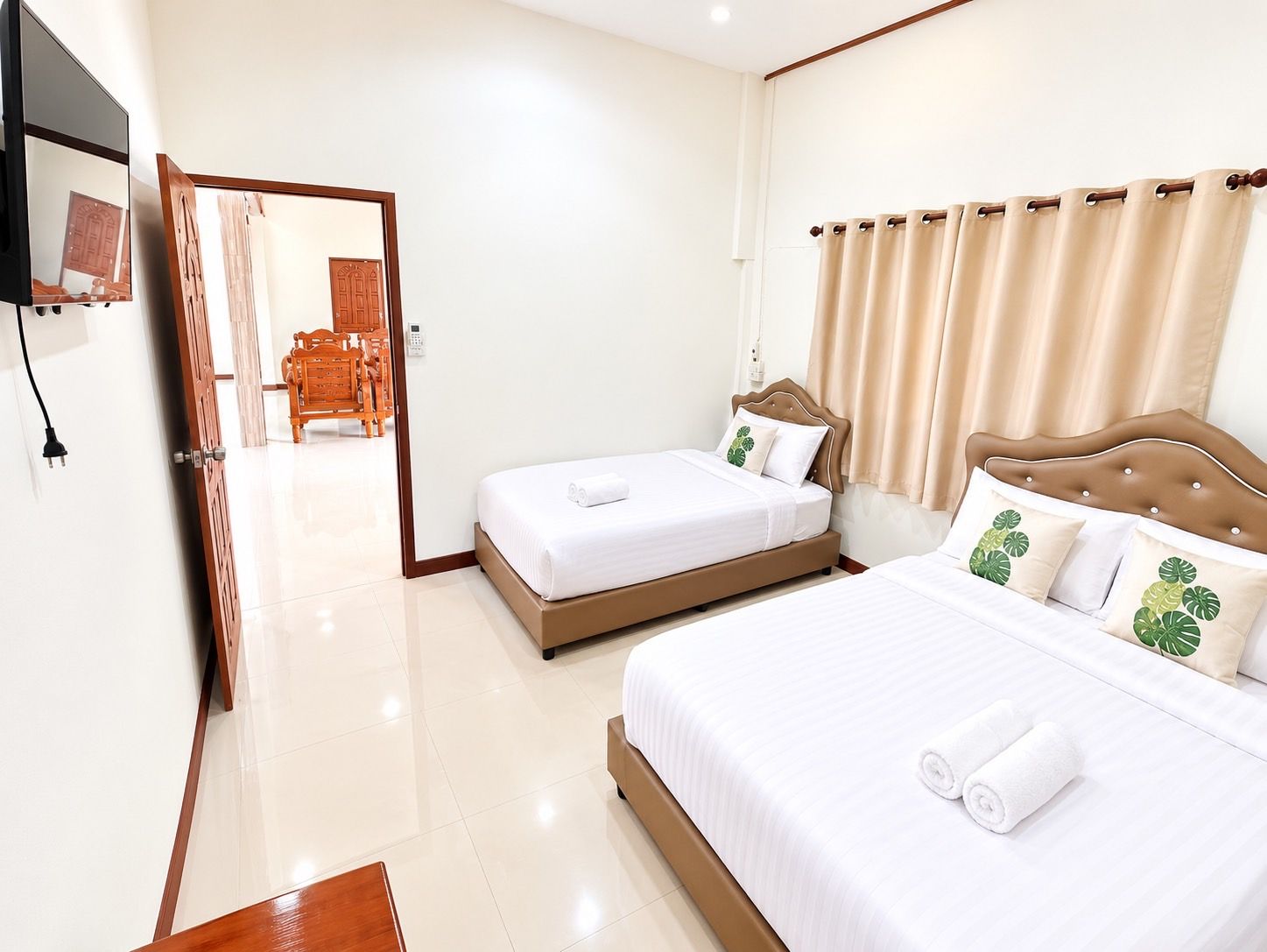 A hotel room with two beds, a wooden headboard, a flat-screen TV, and a bathroom visible through an open door.