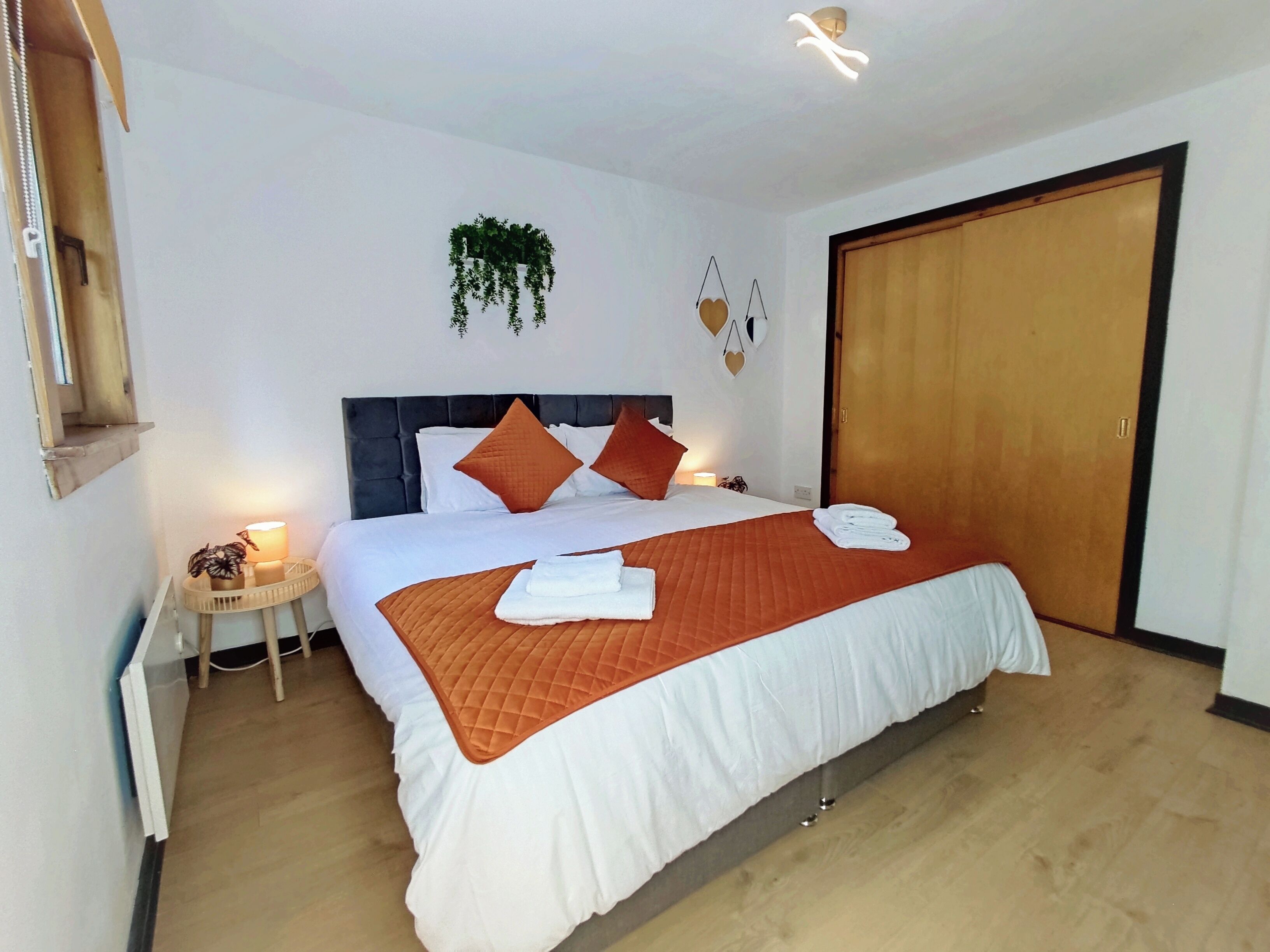 Una cama bien hecha con ropa de cama blanca y naranja, una mesita de noche con una lámpara y una puerta de madera.