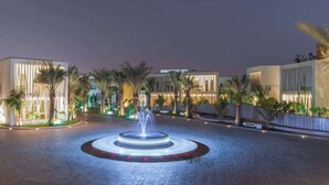 Un hotel moderno con una fuente central, palmeras y senderos bien iluminados.