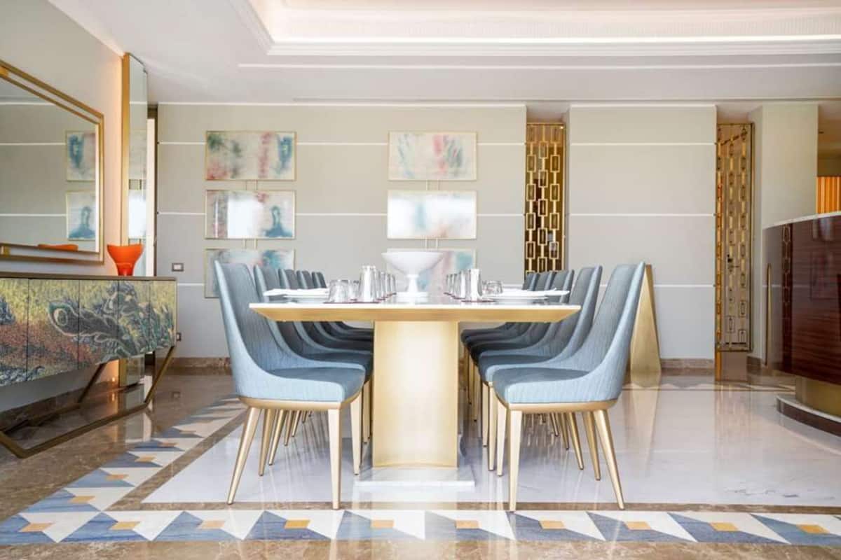A modern dining area with a round table, blue upholstered chairs, and a decorative cabinet.