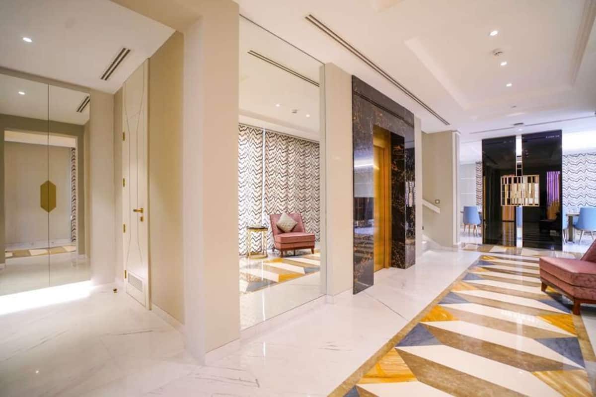 A modern hotel lobby with a marble floor, a patterned rug, and a seating area with a pink sofa.