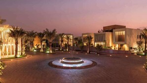 Un patio de hotel moderno con una fuente central, palmeras y edificios contemporáneos.