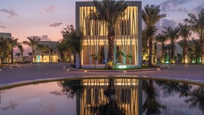 Un hotel moderno con un atrio central, palmeras y una piscina reflectante.