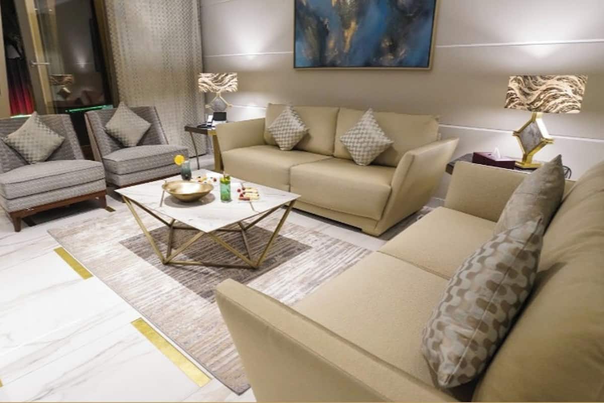 A modern living room with a beige sofa, two armchairs, a coffee table, and a painting on the wall.
