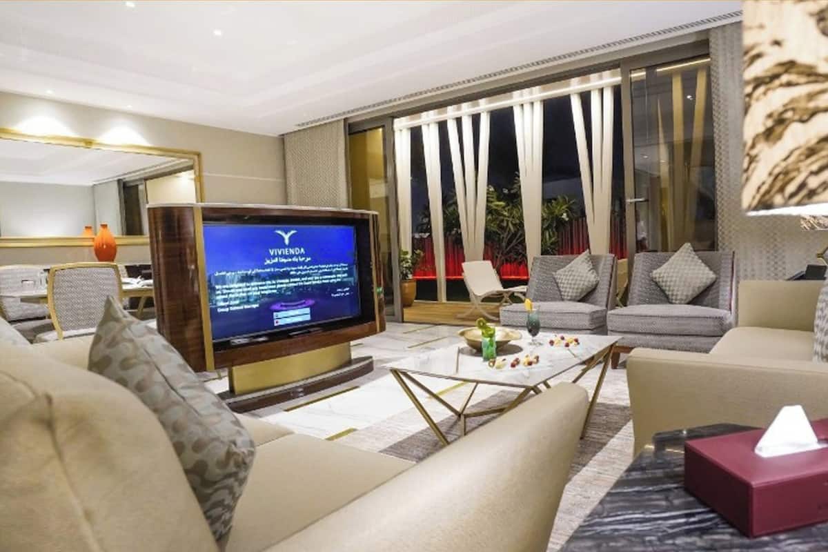 A modern living room with a flat-screen TV, comfortable seating, a coffee table, and a large window with curtains.