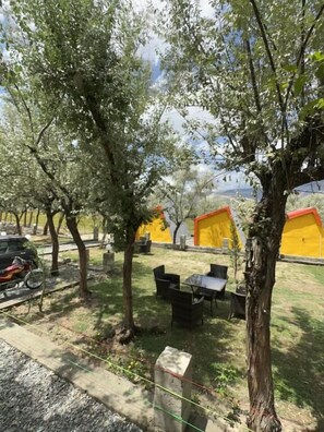 An outdoor seating area with tables and chairs, surrounded by trees and yellow tents. - Montagna PODS (Skardu)