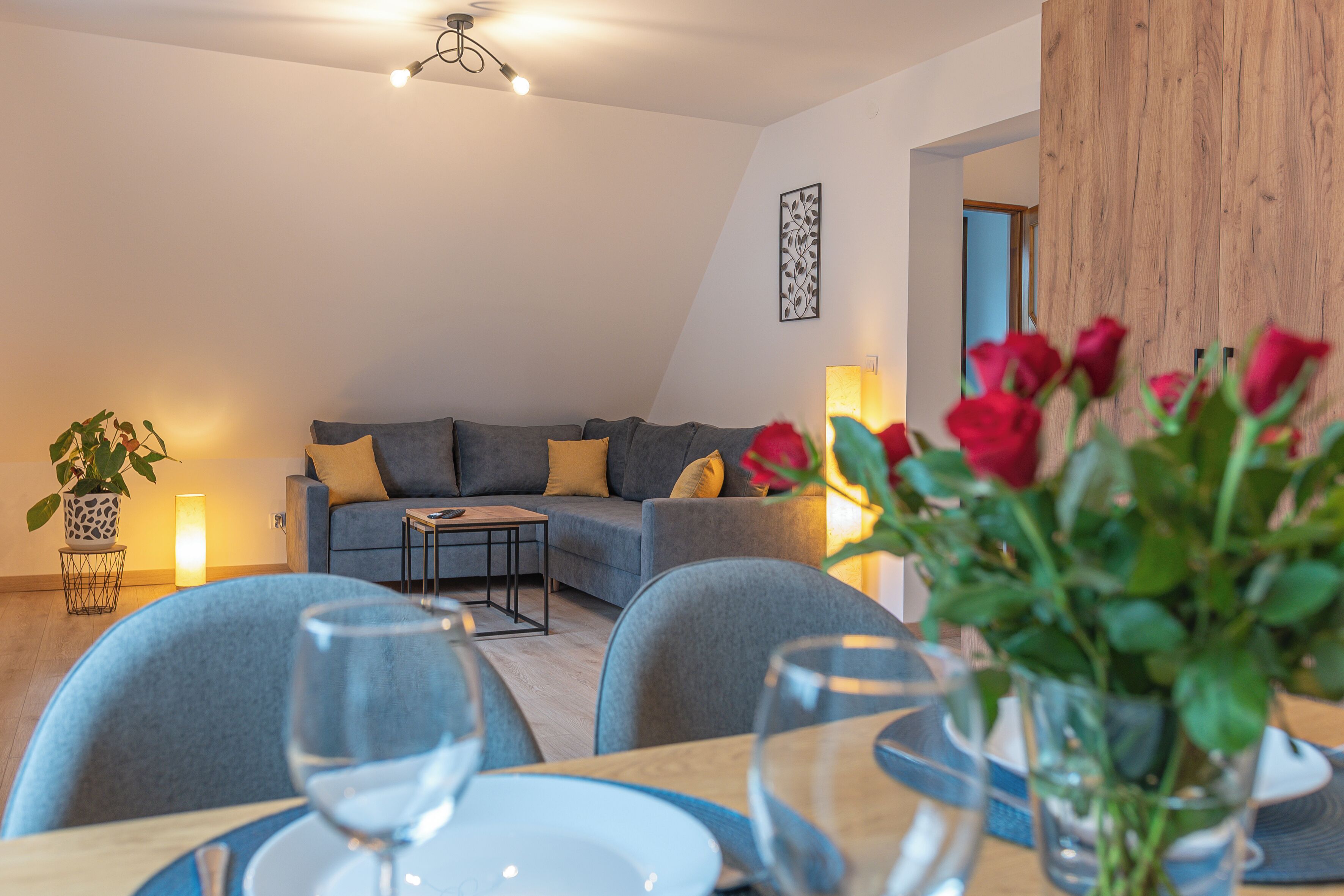 A modern living room with a sofa, a dining table with chairs, and a vase of red flowers.