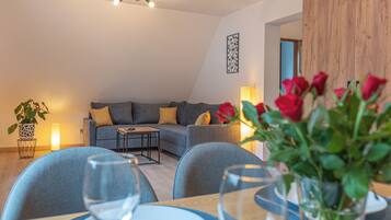 A modern living room with a sofa, a dining table with chairs, and a vase of red flowers.