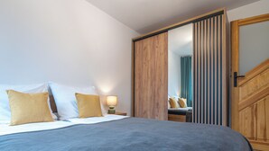 Un dormitorio con una cama, almohadas, una mesita de noche, una lámpara, un armario de madera y un espejo.