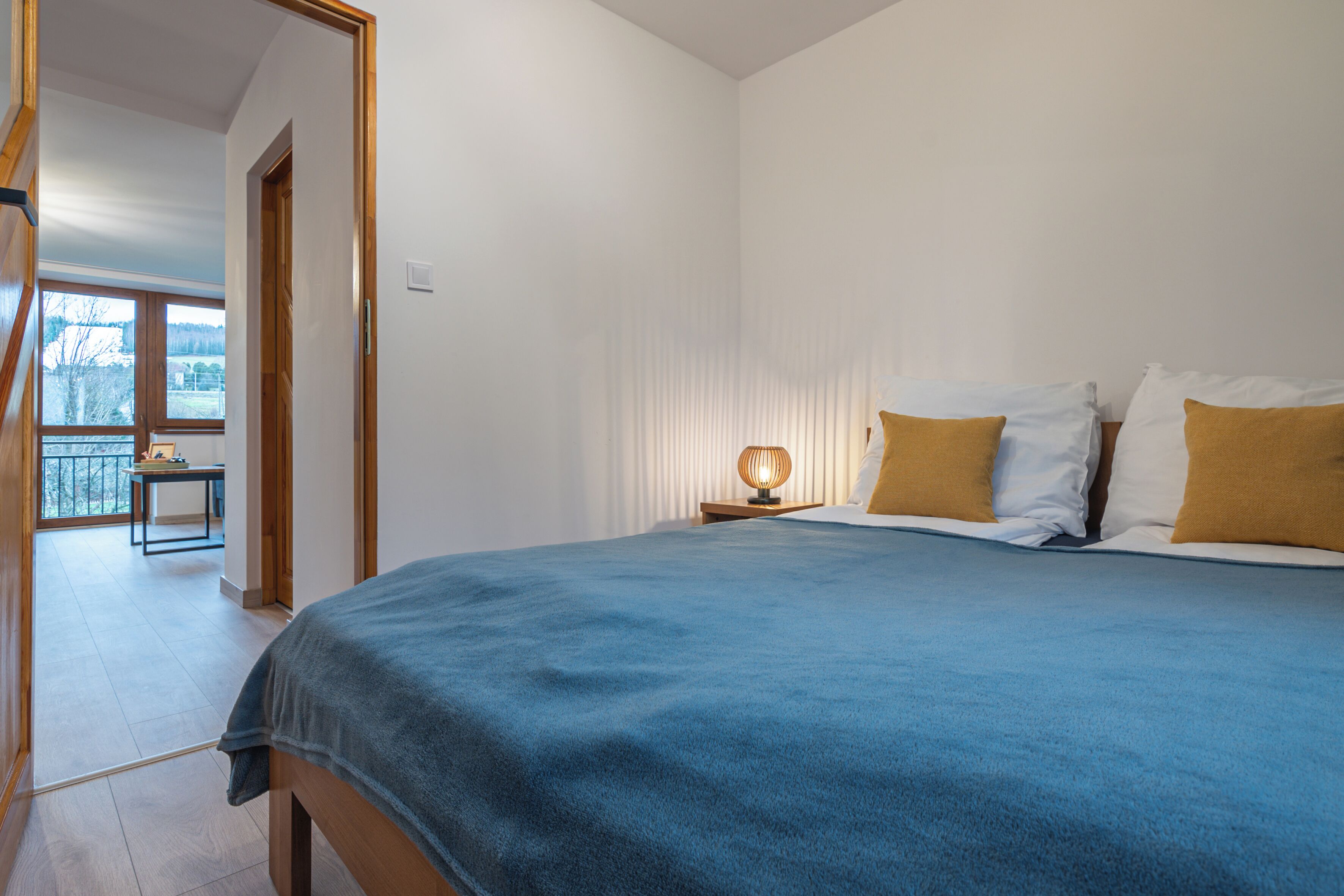 A bedroom with a large bed, a bedside table with a lamp, and a view of a balcony.
