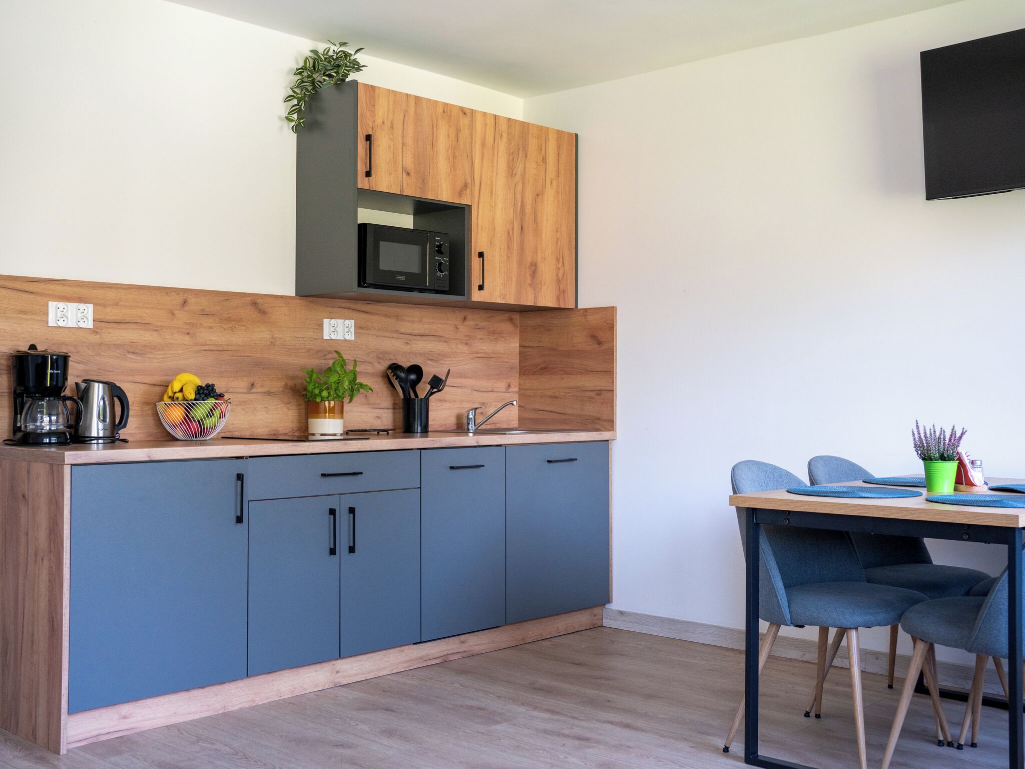 A modern kitchen with grey cabinets, a wooden countertop, a microwave, and a dining area with a table and chairs.