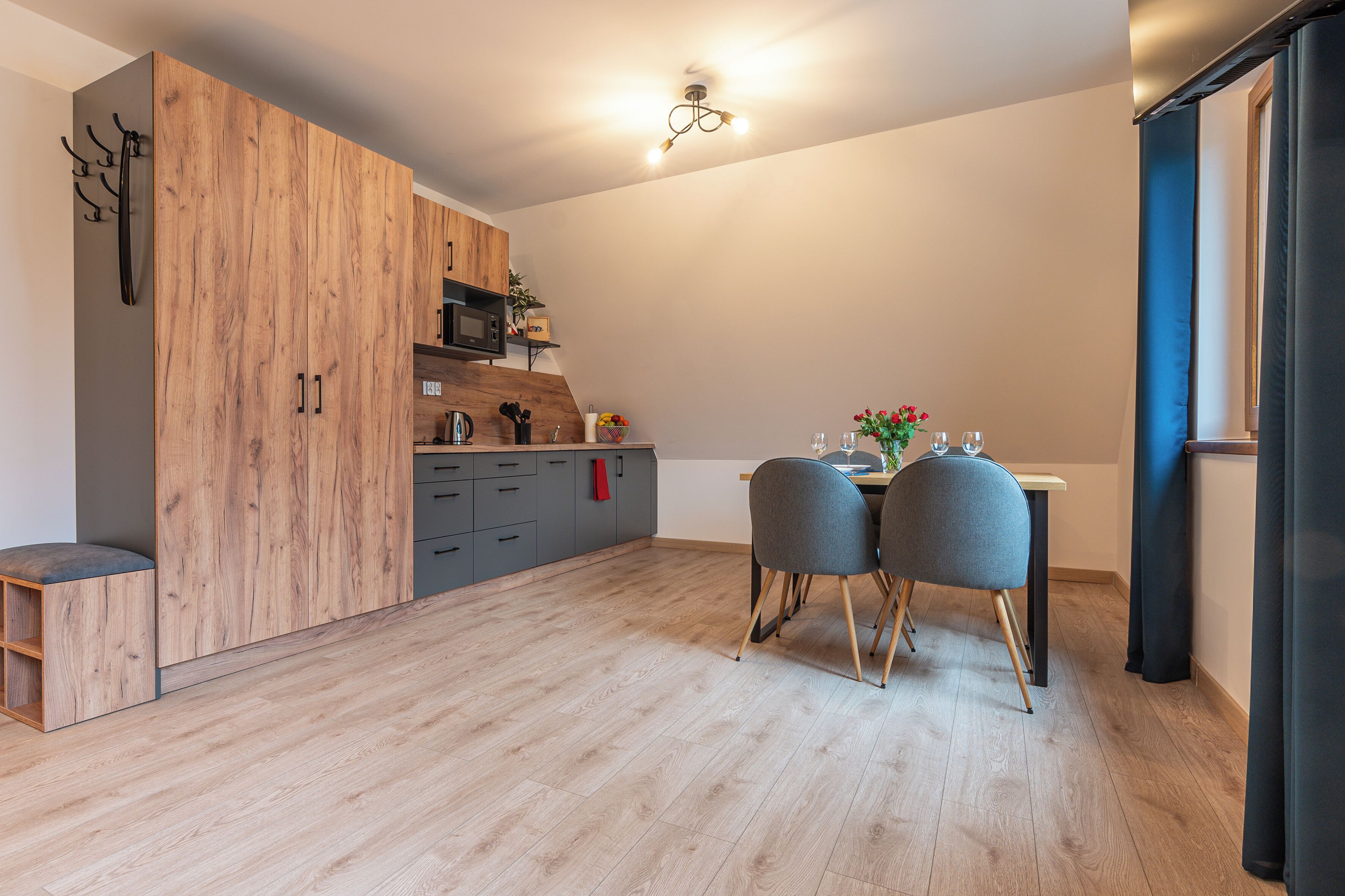 Una cocina moderna con armarios de madera, una mesa de comedor con dos sillas y una pequeña encimera con una tetera y otros objetos.
