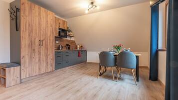 Una cocina moderna con armarios de madera, una mesa de comedor con dos sillas y una pequeña encimera con una tetera y otros objetos.