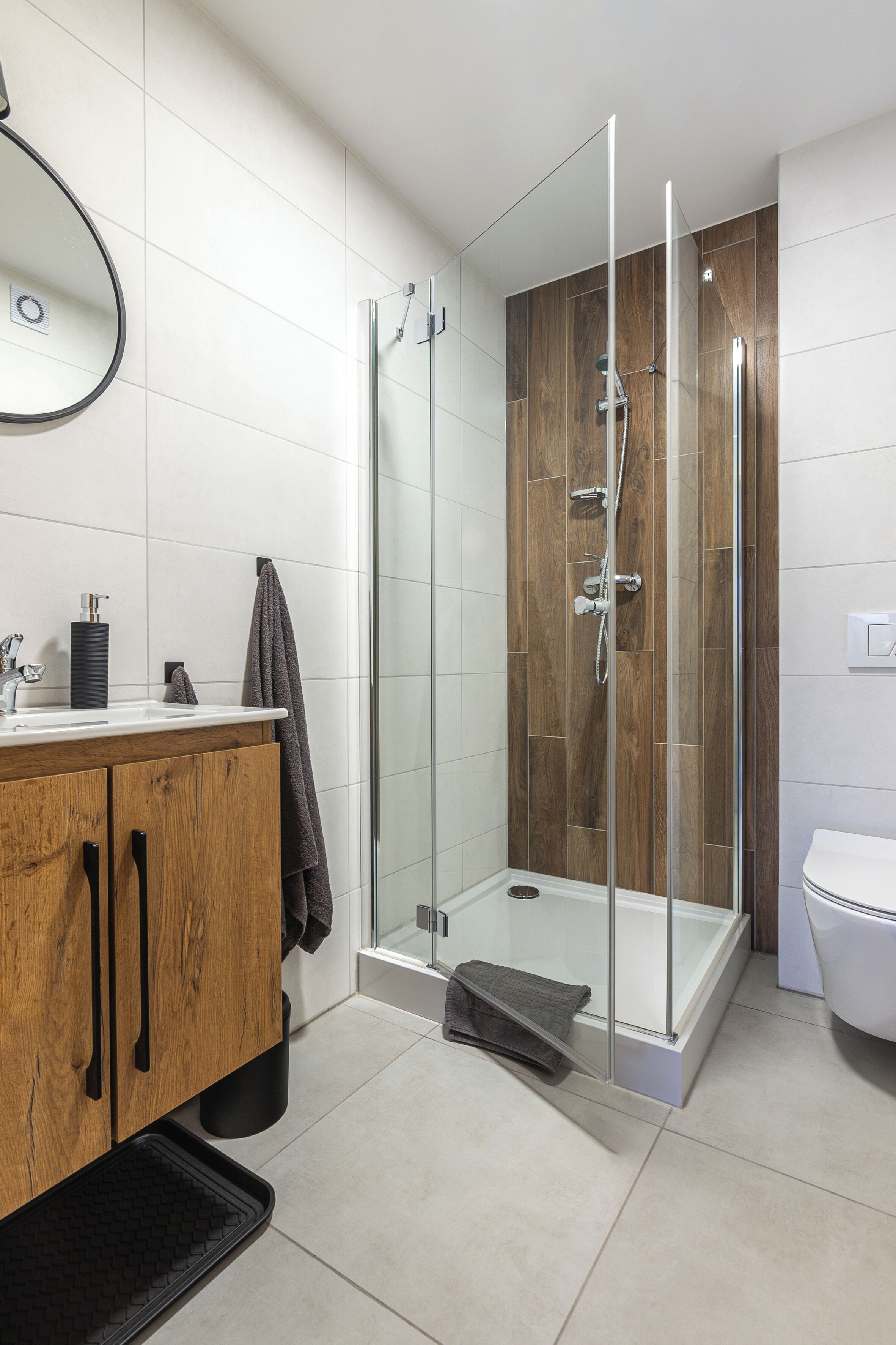 A modern bathroom with a glass-enclosed shower, a wooden vanity, and a white toilet.