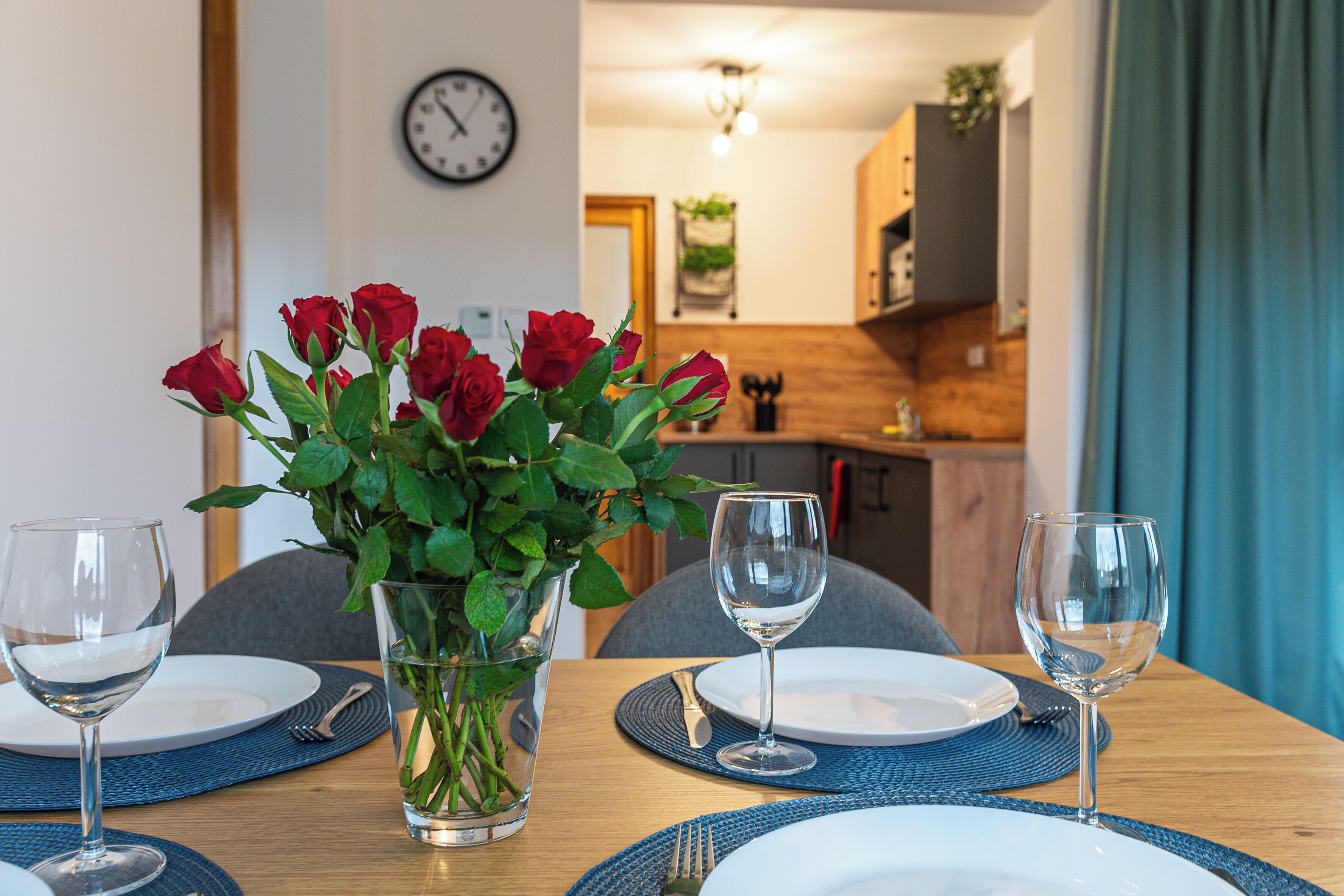 A dining table set with plates, cutlery, and wine glasses, with a vase of red roses in the center.