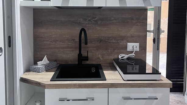 A compact kitchen with a black sink, white cabinets, and a wooden backsplash. - 1 Bedroom Private vacation home in Bari (Bari)