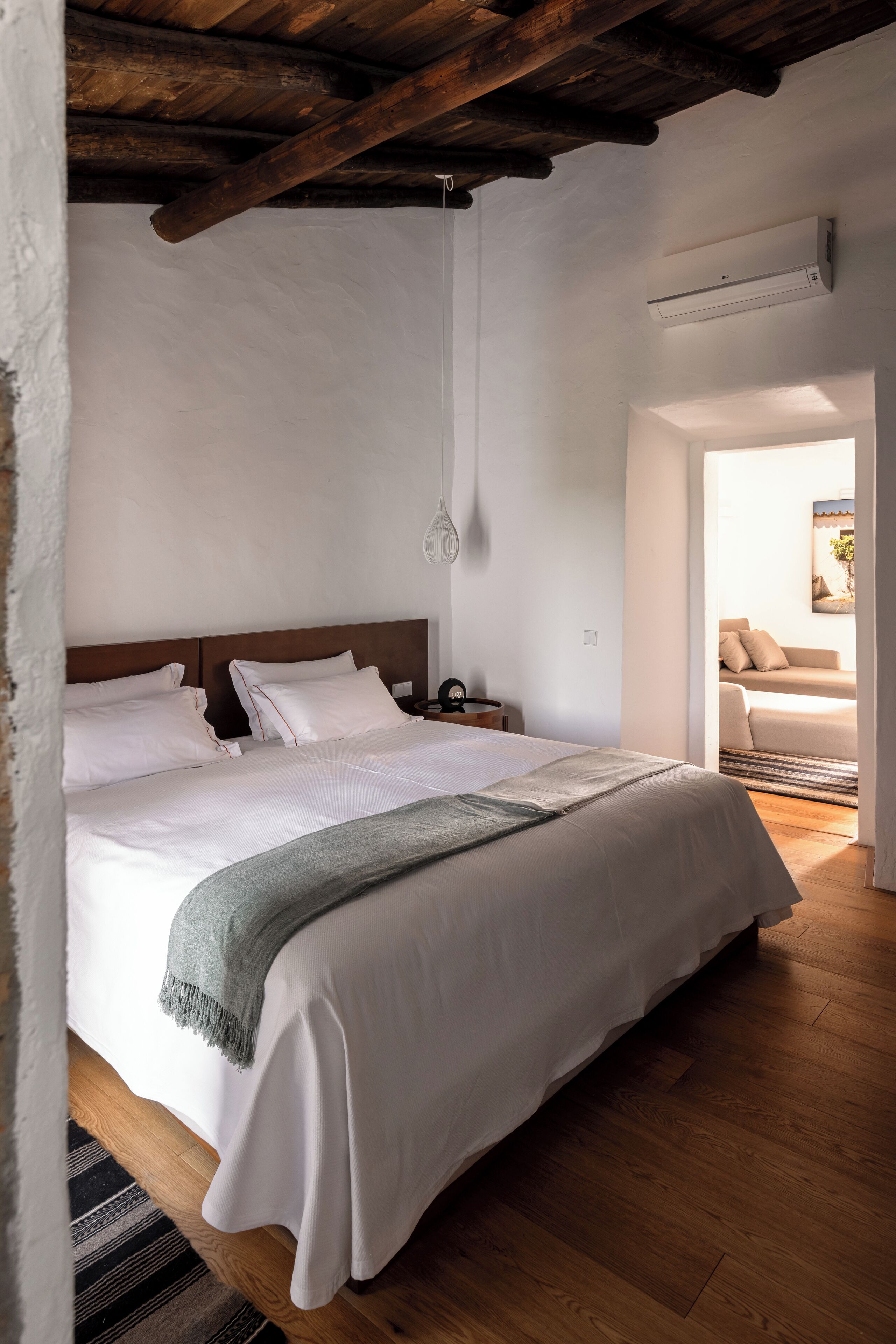 Quarto com teto de madeira, uma cama com roupa de cama branca, mesa de cabeceira e luminária pendente.