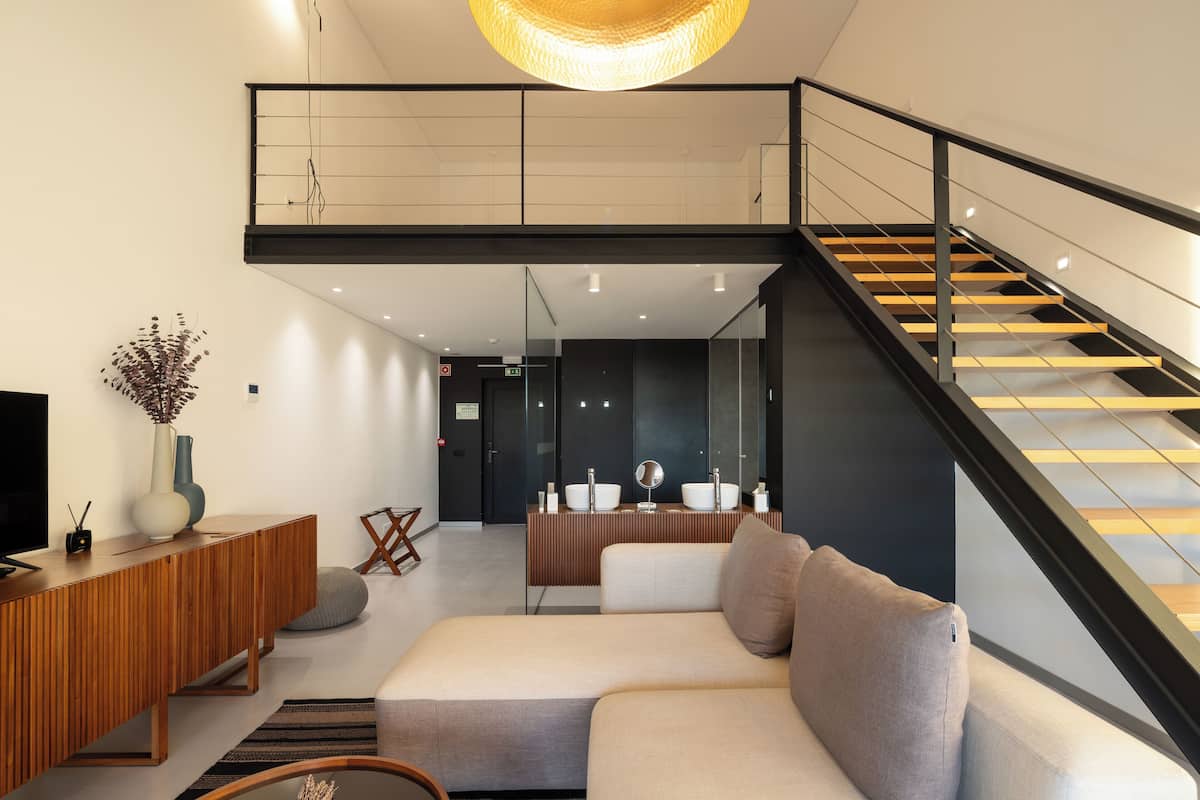 Een moderne woonkamer met een bank, een houten console en een televisie. Een trap met glazen balustrade leidt naar een hoger gelegen verdieping.