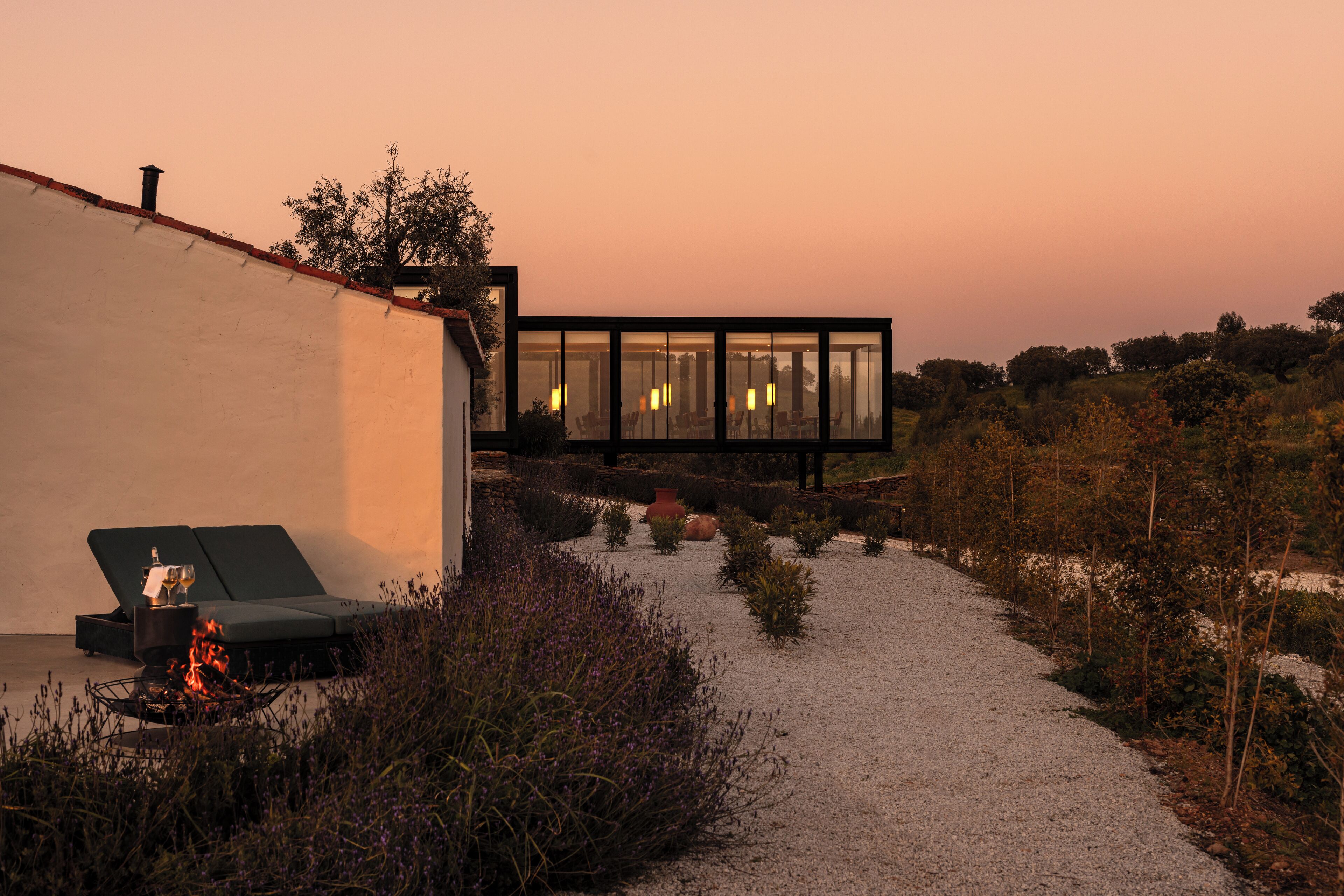 A modern outdoor seating area with a fire feature, a glass-enclosed structure, and a gravel path.
