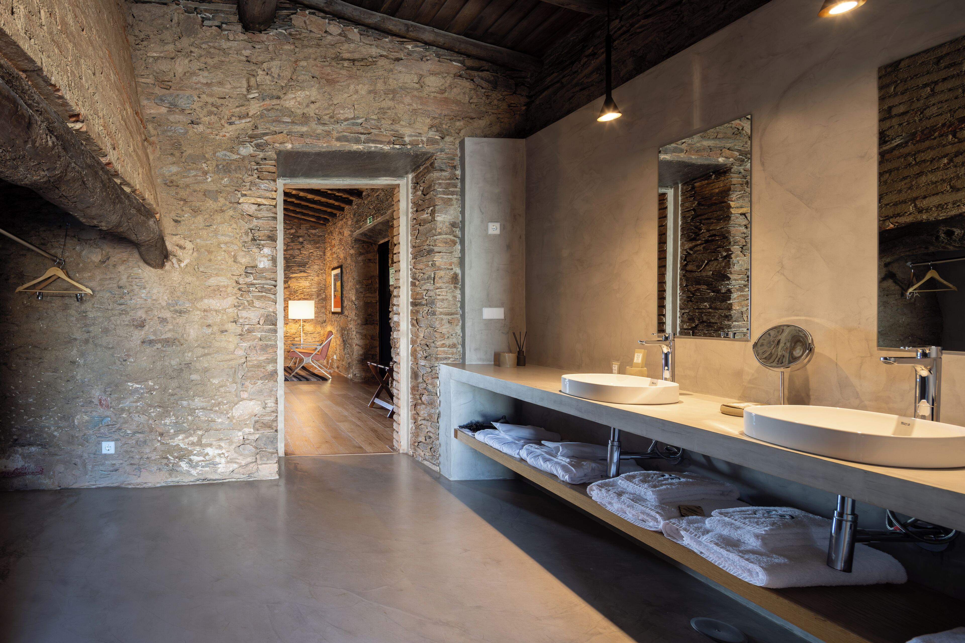 A modern bathroom with a stone wall, a large mirror, a sink, and a towel rack.