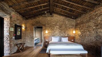Ein rustikales Schlafzimmer mit einer Steinwand, Holzbalkendecke, einem Bett mit weißer Bettwäsche und hängenden Pendelleuchten.