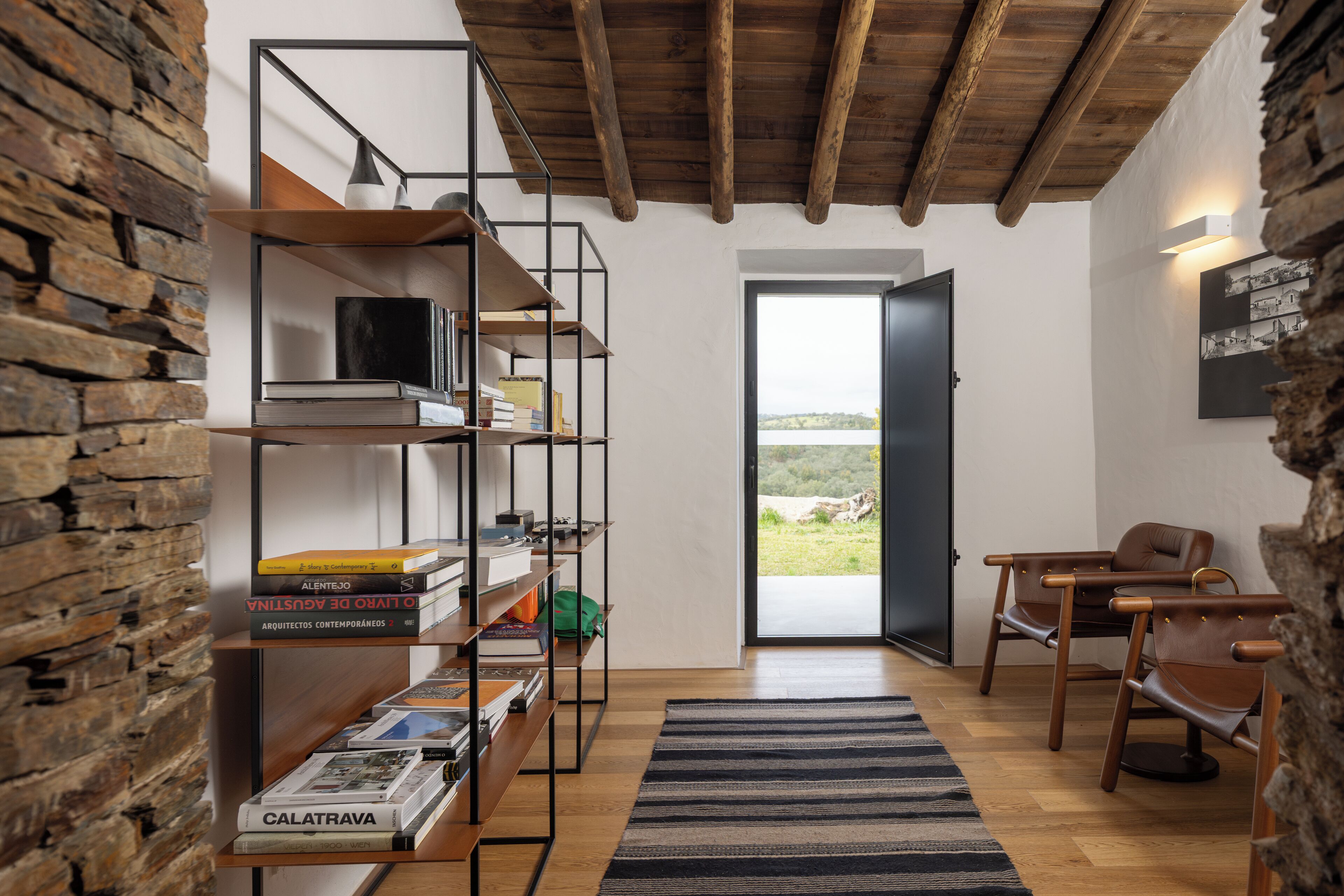 Een modern interieur met een houten boekenkast, lederen fauteuils en een uitzicht door een deur.