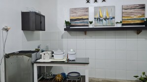 A kitchen with white tiles, a black cabinet, and a countertop with a stove and pots. There are three paintings on the wall above the counter. - Omah Beji di Batu (Batu)