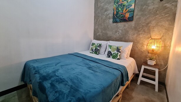 A bedroom with a bed, a nightstand, a wall-mounted lamp, and a painting. - Omah Beji di Batu (Batu)
