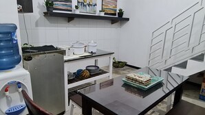 A kitchen with white cabinets, a water dispenser, a refrigerator, a stove, and a dining table with a box of chocolates. - Omah Beji di Batu (Batu)