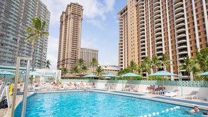 A swimming pool with lounge chairs and umbrellas, surrounded by tall residential buildings.