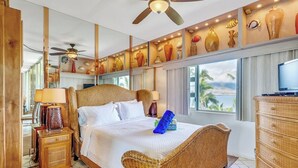 A hotel room with a large bed, a ceiling fan, a TV, and a view of palm trees.