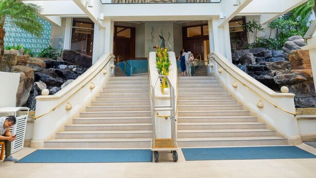 A spacious lobby with a central staircase, a glass ceiling, and a view of the upper floors.
