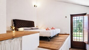 Une chambre à coucher avec un lit, une table de chevet, une lampe et une fenêtre donnant sur un paysage verdoyant.