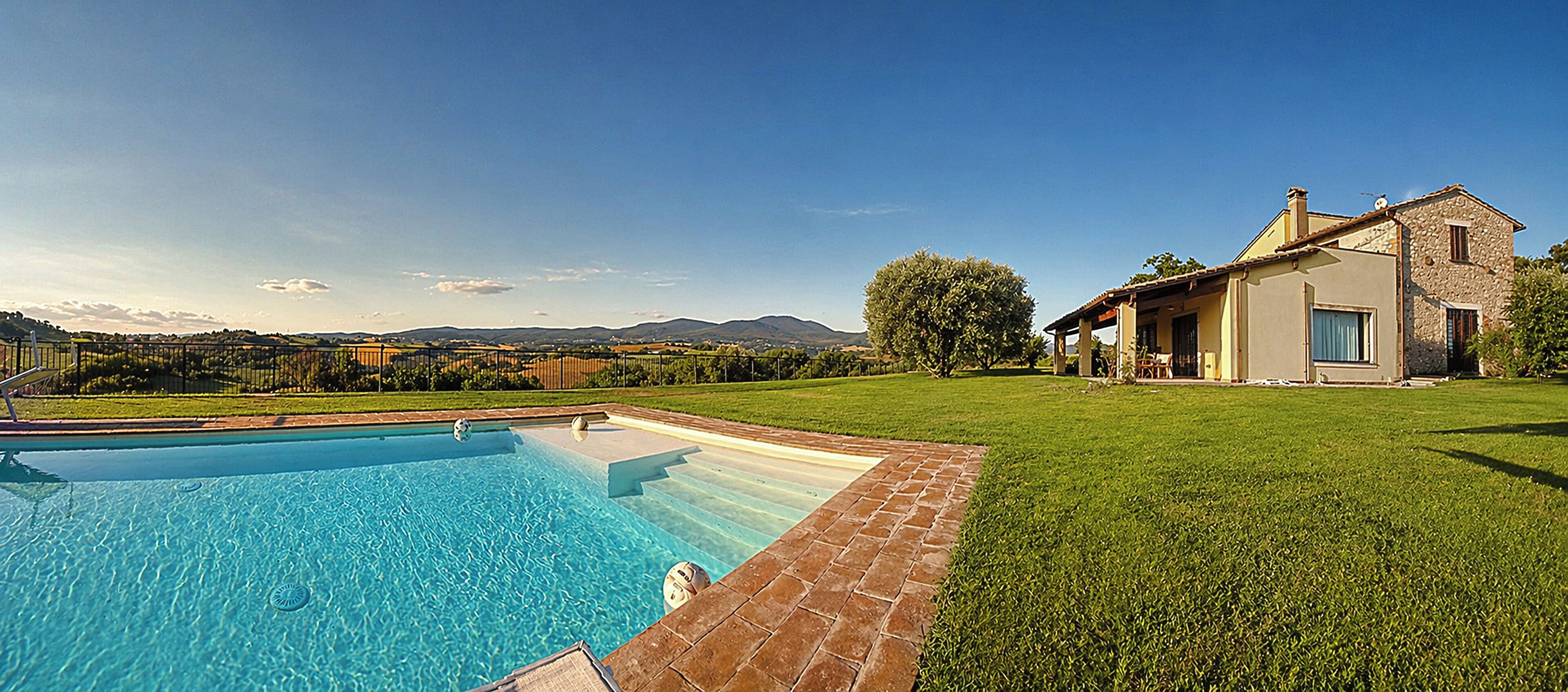 A swimming pool with a brick border, a grassy lawn, and a stone building with a window.