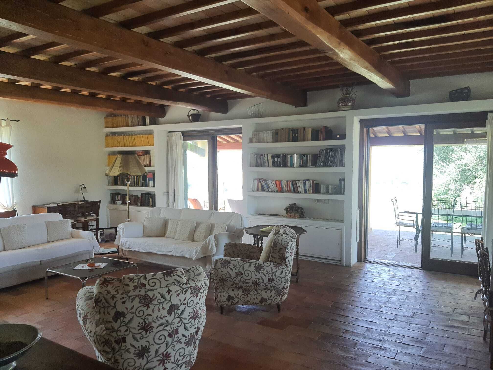 A spacious living room with a white sofa, patterned armchairs, a coffee table, and a bookshelf filled with books.