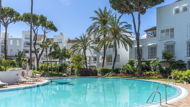 A swimming pool surrounded by palm trees and white buildings with balconies. - Housing White Pearl Beach by Sharing Co (Marbella)
