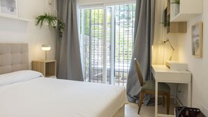 A hotel room with a bed, a desk, a chair, a lamp, a plant, and a view through the window. - Housing White Pearl Beach by Sharing Co (Marbella)