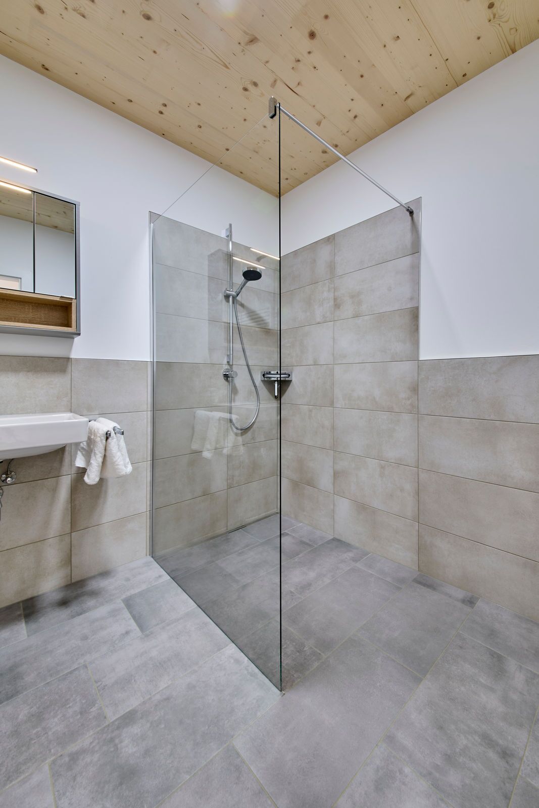 A modern bathroom with a glass-enclosed shower, a wooden ceiling, and a white sink with a towel.