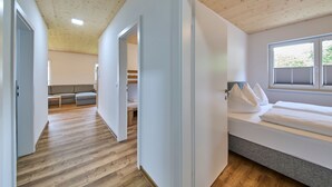 Una habitación moderna con techo de madera, cama con ropa de cama blanca, ventana con persianas y un sofá al fondo.