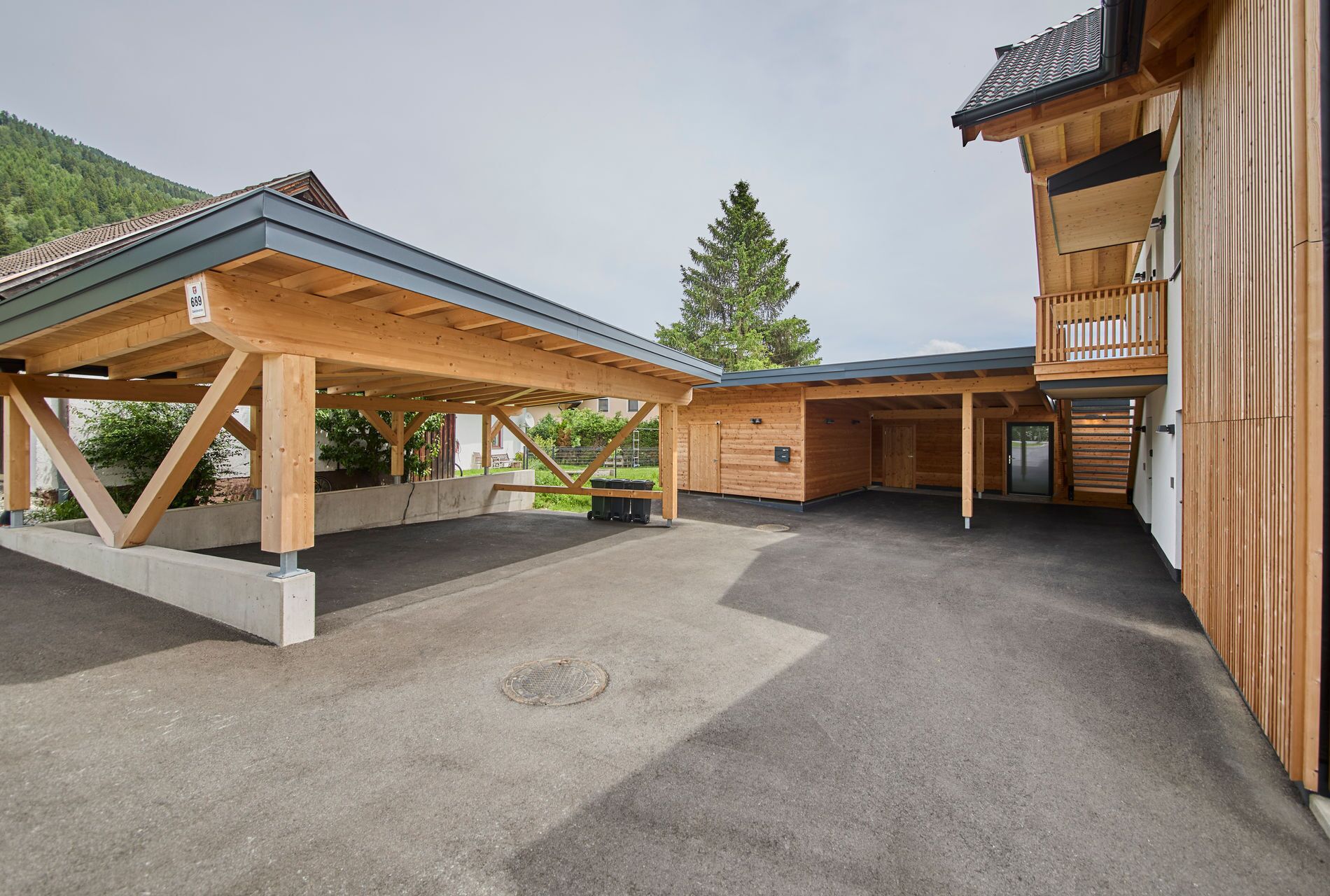 A covered outdoor area with a wooden structure, a concrete floor, and a building with a balcony.