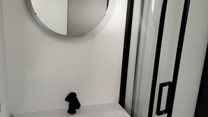 Une salle de bain avec un lavabo blanc, un miroir rond et un robinet noir. Il y a deux tiroirs sous le lavabo.