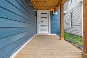 A wooden deck leading to a white door with three windows, surrounded by blue siding. - Farm House DT Indy with Pool Table (Indianapolis)