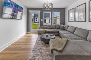 Un salon moderne avec un canapé d’angle, une table basse ronde et un téléviseur à écran plat fixé au mur.