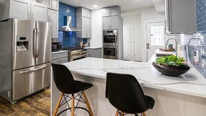 A modern kitchen with stainless steel appliances, a white island with bar stools, and a blue-tiled backsplash. - Historic Fountain Sq in DT Indy (Indianapolis)