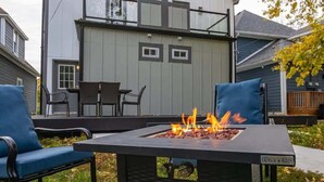A square outdoor fire pit with a metal frame and a label, surrounded by two blue chairs. - Historic Fountain Sq in DT Indy (Indianapolis)