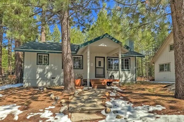 A cabin with a porch, surrounded by trees and a stone pathway.