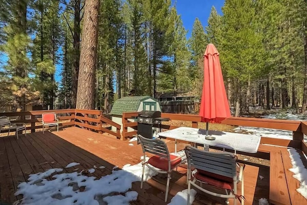 Une terrasse en bois avec une table et des chaises, entourée de grands arbres.