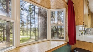 A cabin interior with large windows, a kitchen area, and a view of a forest.